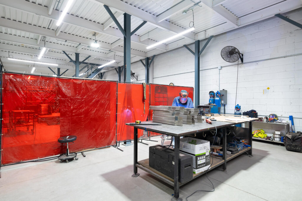 "Worker in protective gear at ATH fabrication workshop behind a red safety curtain"